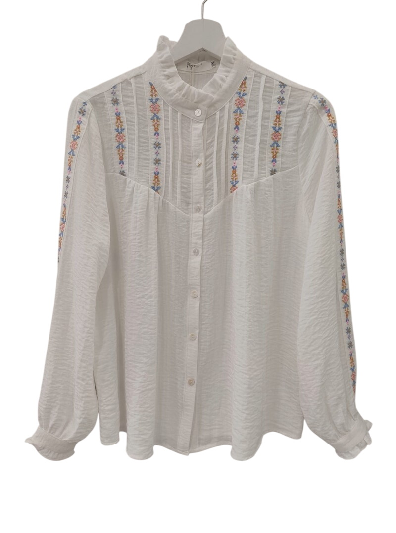 Camisa blanca de chica con bordados de punto de cruz multicolores en mangas y parte superior, cuello alto fruncido, tejido de