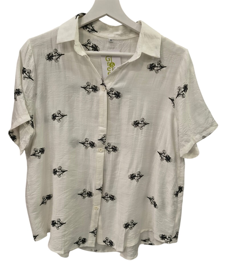 Camisa de manga corta para chica en color blanco, corte holgado, con flores bordadas negras sobre fondo claro y cuello de sol